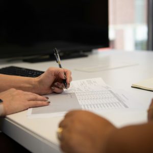 Two people sitting at a desk writing on a piece of paper, working through paperwork together