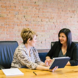 Two women seated on leather chairs in front of a table, as in a one-to-one coaching session
