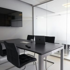 Small empty meeting room with a table, chairs, a television screen and a laptop, ready for a team session