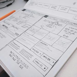 Hand-drawn website wireframe on paper with an orange pen on a desk